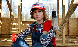 a female construction worker, holding an electric screw-driver pointing up towards the sky